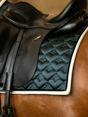 Side view of a chestnut horse wearing the green PS of Sweden Heart Dressage Saddle Pad under a black saddle