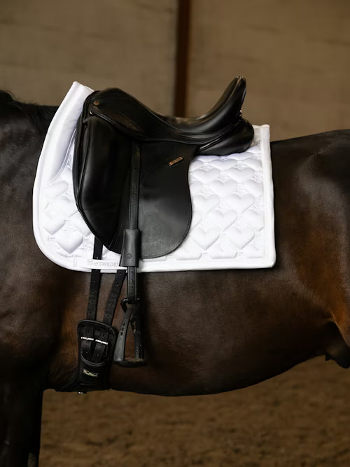 Side view of a black horse wearing the white PS of Sweden Heart Dressage Saddle Pad under a black saddle