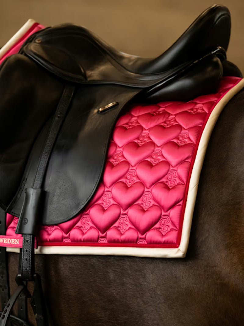 Side view of a black horse wearing the pink PS of Sweden Heart Dressage Saddle Pad under a black saddle