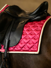Side view of a black horse wearing the pink PS of Sweden Heart Dressage Saddle Pad under a black saddle