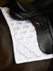 Side view of a black horse wearing the white PS of Sweden Heart Dressage Saddle Pad under a black saddle