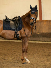 Side view of a chestnut horse wearing the navy PS of Sweden Heart Dressage Saddle Pad under a black saddle