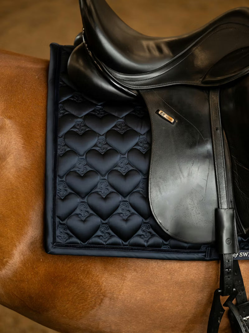 Side view of a chestnut horse wearing the navy PS of Sweden Heart Dressage Saddle Pad under a black saddle