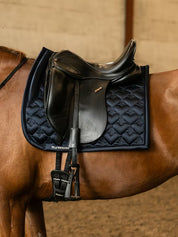 Side view of a chestnut horse wearing the navy PS of Sweden Heart Dressage Saddle Pad under a black saddle