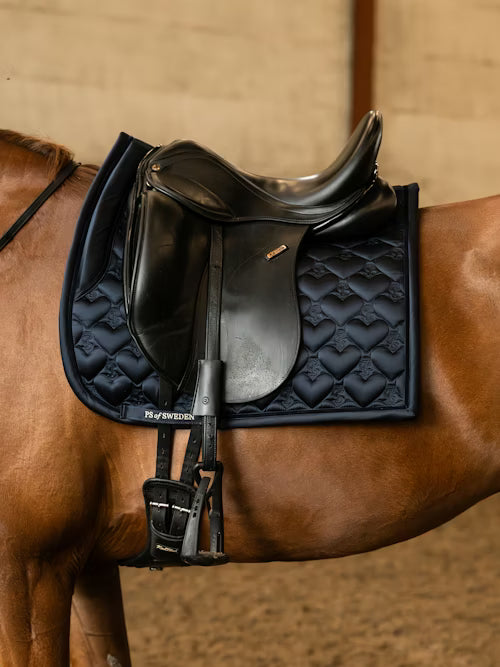 Side view of a chestnut horse wearing the navy PS of Sweden Heart Dressage Saddle Pad under a black saddle