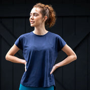 Front view of a female model wearing the navy Aubrion React Tech T-Shirt while standing in front of a dark colored barn