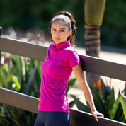 Angled front view of a female model wearing the pink Aubrion React Short Sleeve Base Layer while leaning against a brown fence
