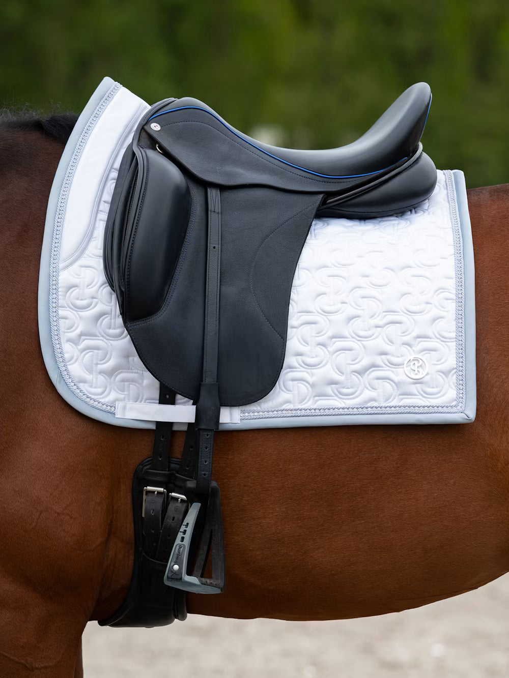 Side view of the white PS of Sweden Crystal Satin Dressage Saddle Pad under a black saddle worn by a bay horse