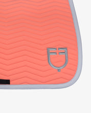Clos up view of the silver logo on the Equestro Wave Quilting Jumping Saddle Pad In Technical Fabric in a coral color on a white background