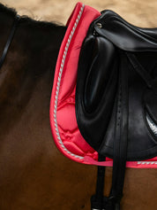 Side view of a horse wearing the pink guava PS of Sweden The Original Monogram Dressage Saddle Pad under a black dressage saddle