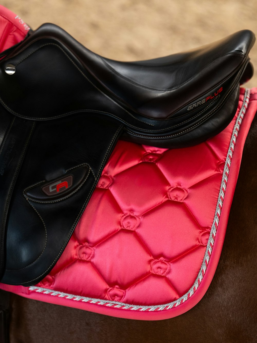 Close-up view of the back of the Pink Guava PS of Sweden The Original Monogram Jump Saddle Pad under a brown saddle