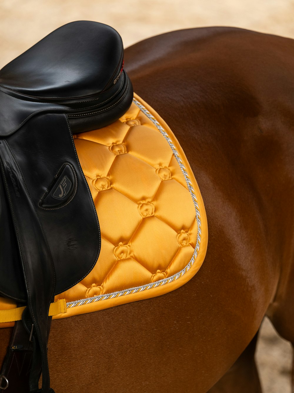 Close-up view of the back of the Sunburst Sorbet PS of Sweden The Original Monogram Jump Saddle Pad under a brown saddle