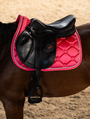 Side view of a horse wearing the Pink Guava PS of Sweden The Original Monogram Jump Saddle Pad under a brown saddle