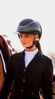 Front view of a female model wearing the anthracite Star Lady Pure Shine Helmet while walking next to a horse
