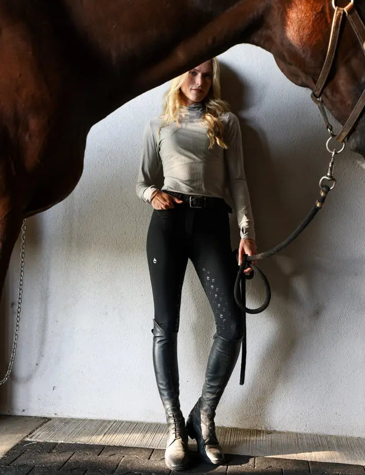 Front view of a model wearing the black Criniere Alice Full Seat Lightweight Full Seat Breeches while holding a horse on a lead rope