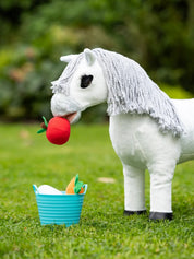 Side view of a white stuffed toy pony standing outside eating a stuffed apple from the blue LeMieux Toy Pony Treat Bucket