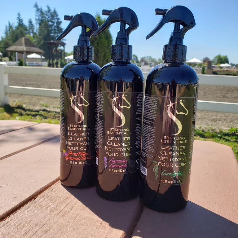 Front view of 3 16oz bottles, each with a different scent, of Sterling Essentials Leather Cleaner with an outdoor arena in the background