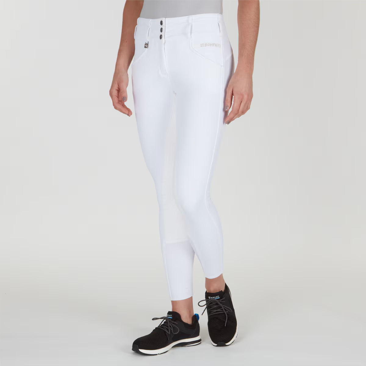 Angled front view of a model wearing the white Romfh Champion Full Seat Breech and black tennis shoes on a plain background