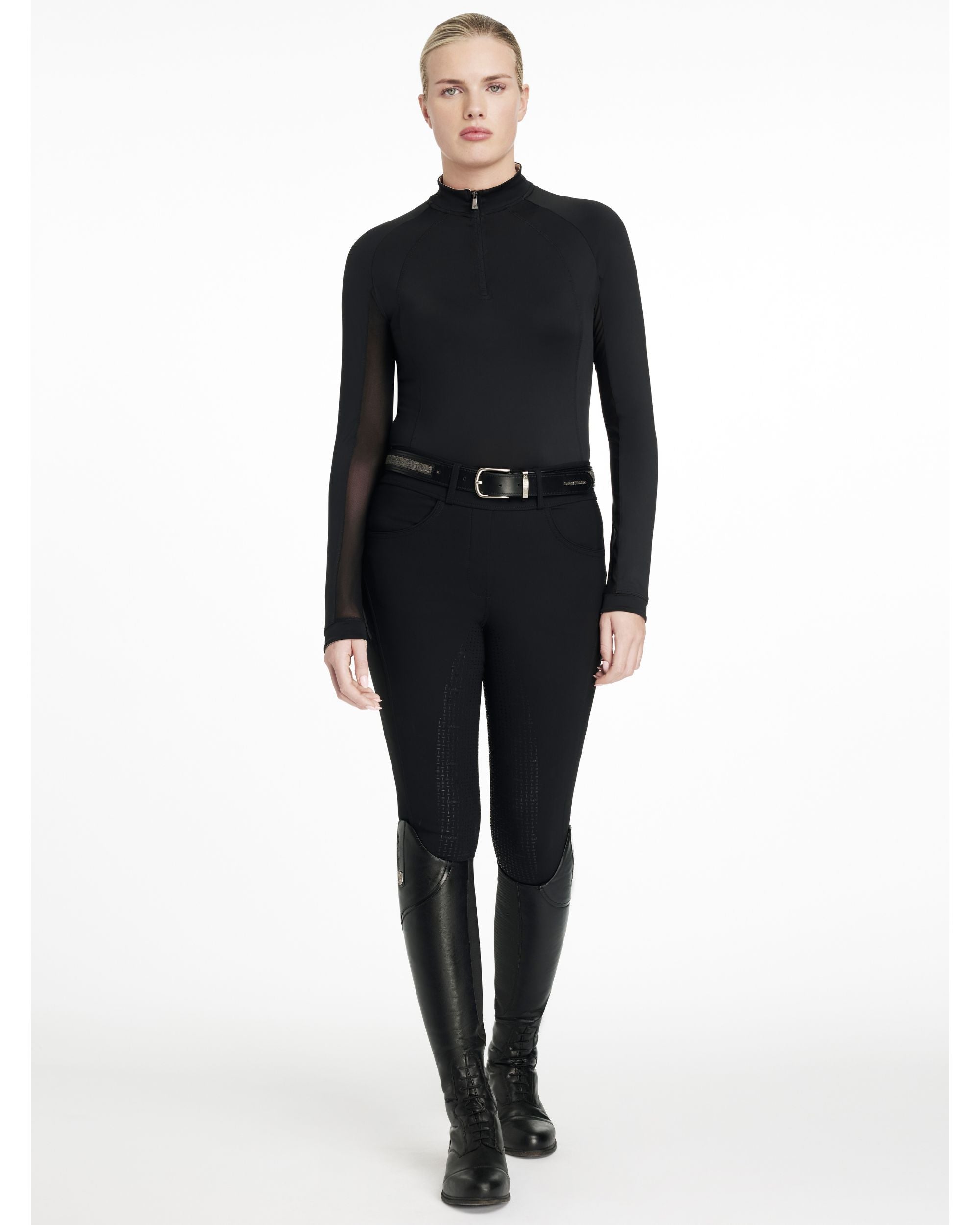 Full body view of a model wearing the black LeMieux Halle Lightweight Base Layer, black breeches, and black tall boots on a white background