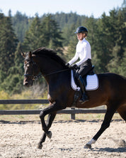 Side view of a female model wearing the black Kerrits Crossover II Full Seat Breech while riding a horse in an outdoor arena