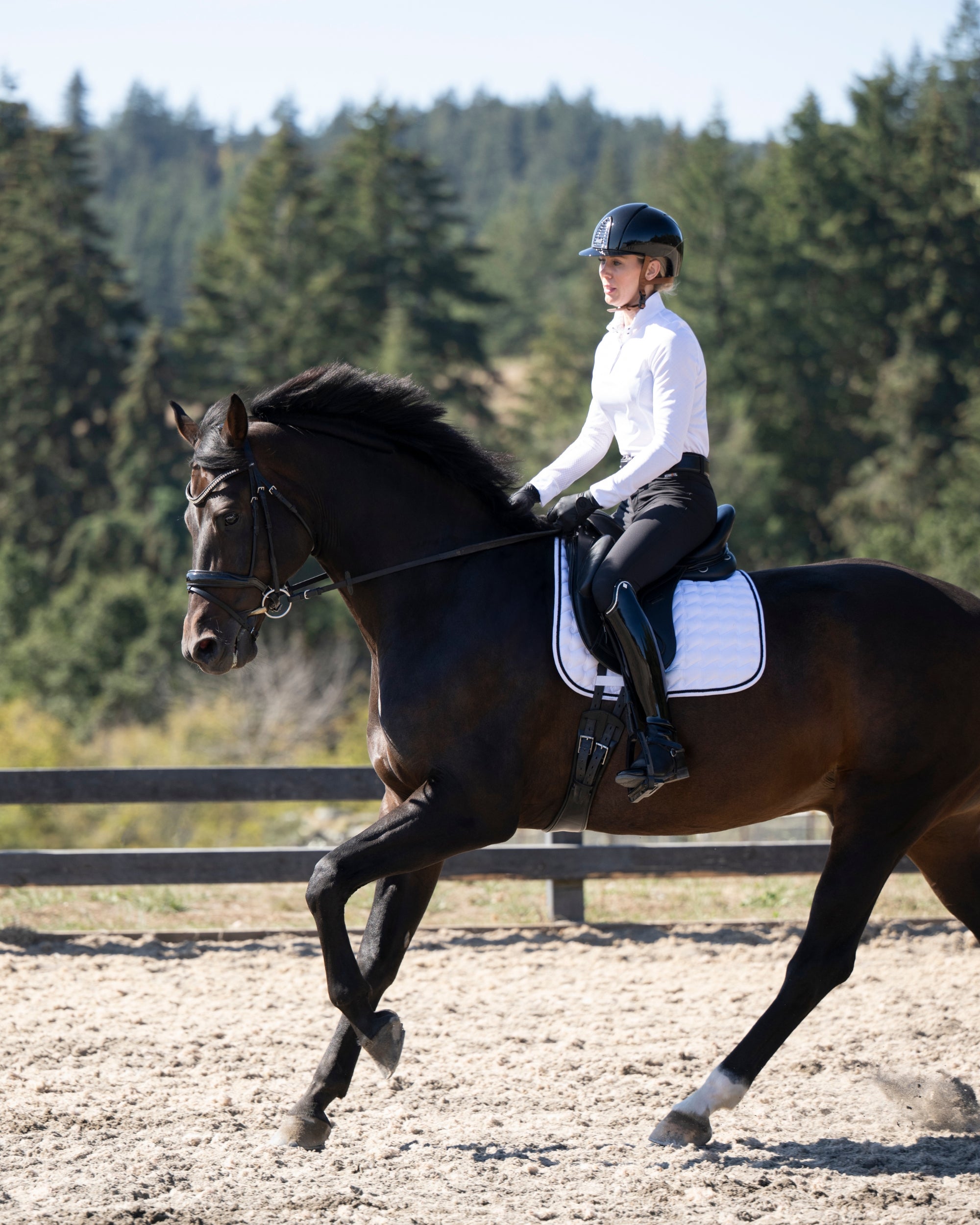 Side view of a female model wearing the black Kerrits Crossover II Full Seat Breech while riding a horse in an outdoor arena