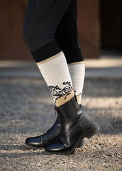 Side view of a model wearing a pair of Kerrits Frolic Horse Knee-Hi Socks in the color Tan