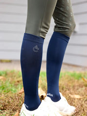 Side view of a model wearing the navy Criniere Equestrian Socks with white sneakers while standing in the grass