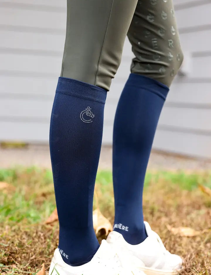 Side view of a model wearing the navy Criniere Equestrian Socks with white sneakers while standing in the grass