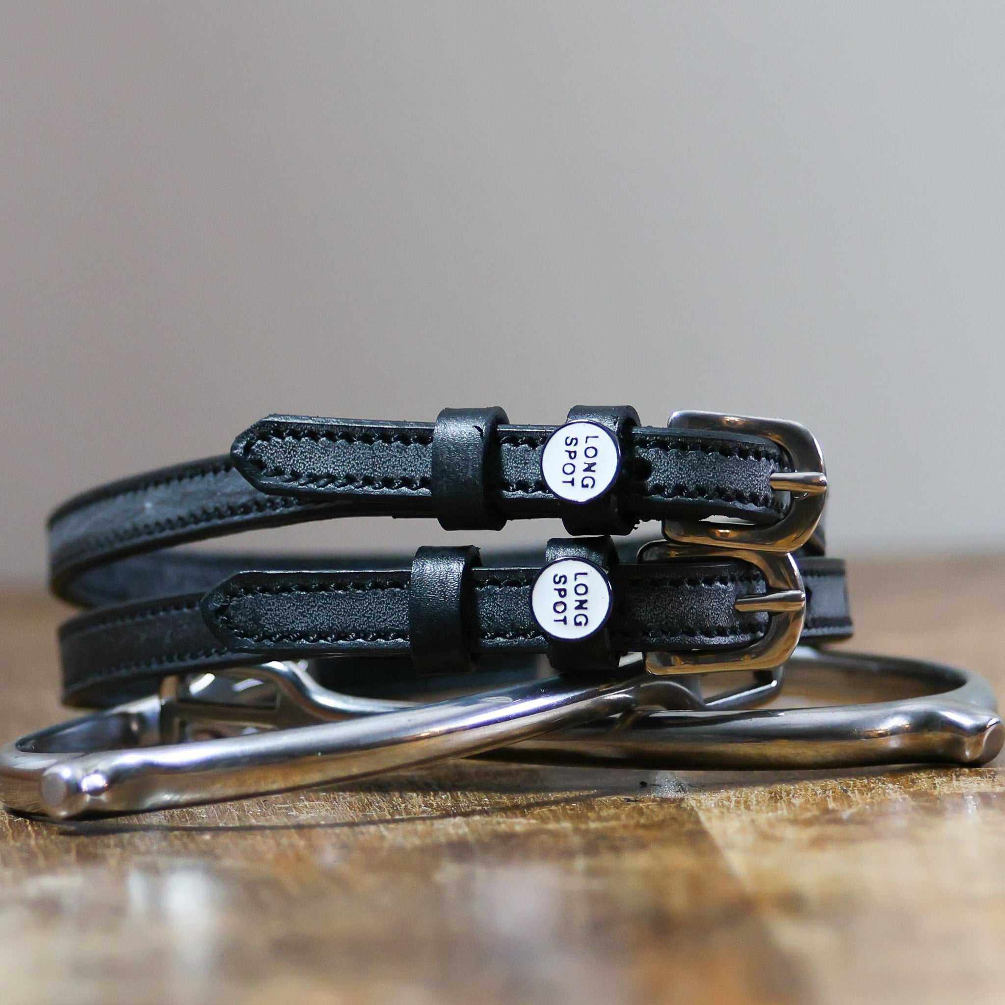 Front view of the buckled Long Spot Mane Jane Spur Straps on wood