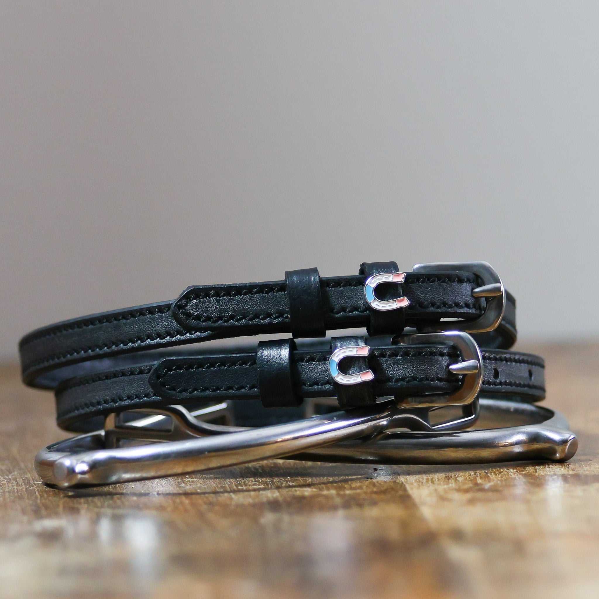 Front view of the buckled Horse Shoe Party Mane Jane Spur Straps on wood