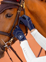 View of a model adjusting the cheekpiece on a bridle on a horse while the model is wearing the navy LeMieux 3D Mesh Riding Gloves