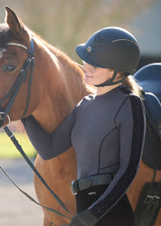 Side view of a female model wearing the Carbon Kerrits Bit of Base Layer Top while standing next to a horse