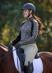Angled front view of a female model wearing the Black Wrought Iron Horse Kerrits Traverse Quarter Zip Fleece Tech Top  while riding a horse outside