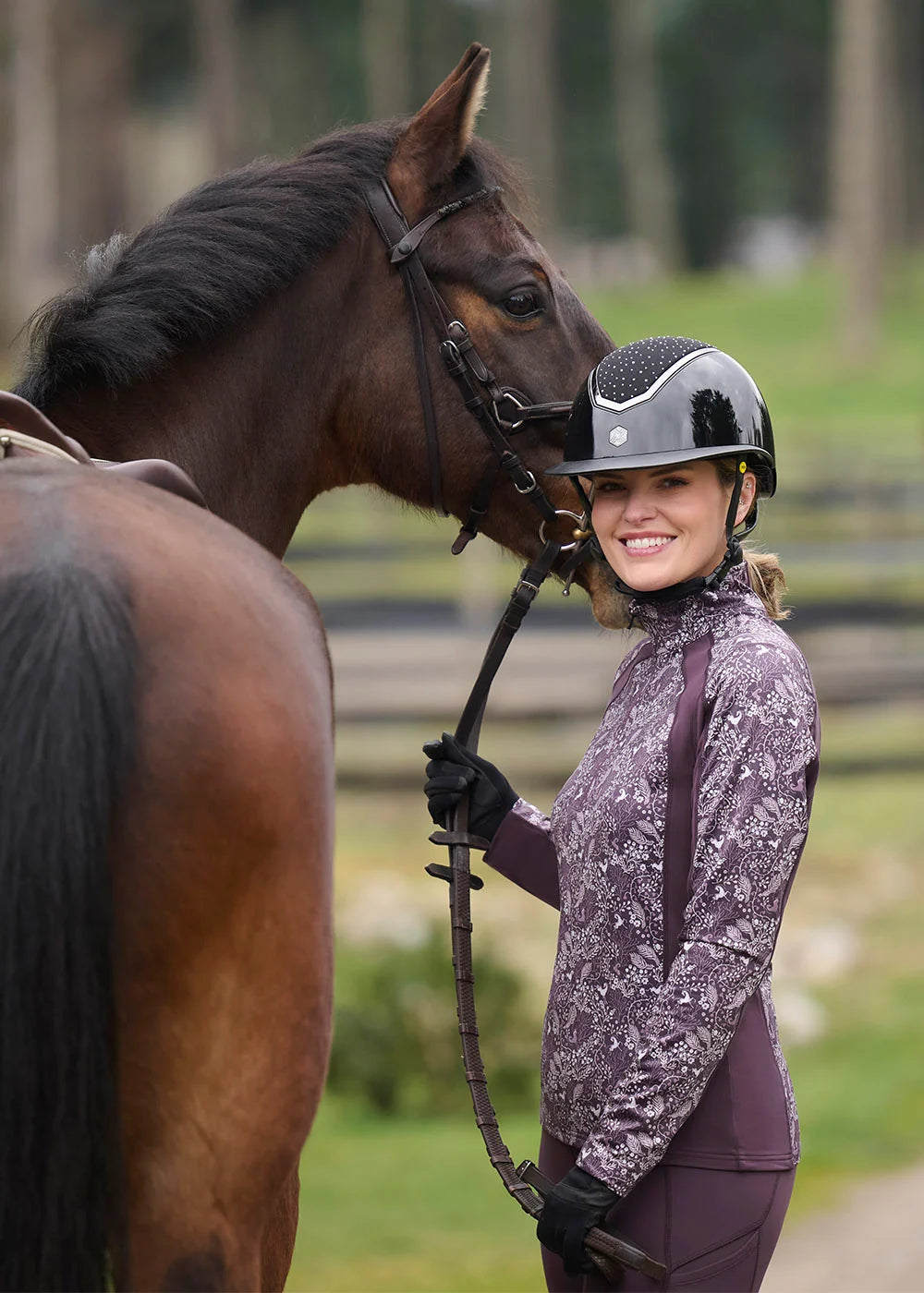 Side view of a female model wearing the Elderberry Fantasy Fillies Kerrits Traverse Quarter Zip Fleece Tech Top  while standing next to a bay horse outside