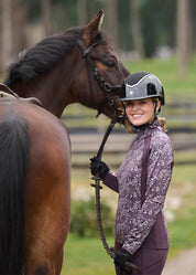 Side view of a female model wearing the Elderberry Fantasy Fillies Kerrits Traverse Quarter Zip Fleece Tech Top  while standing next to a bay horse outside