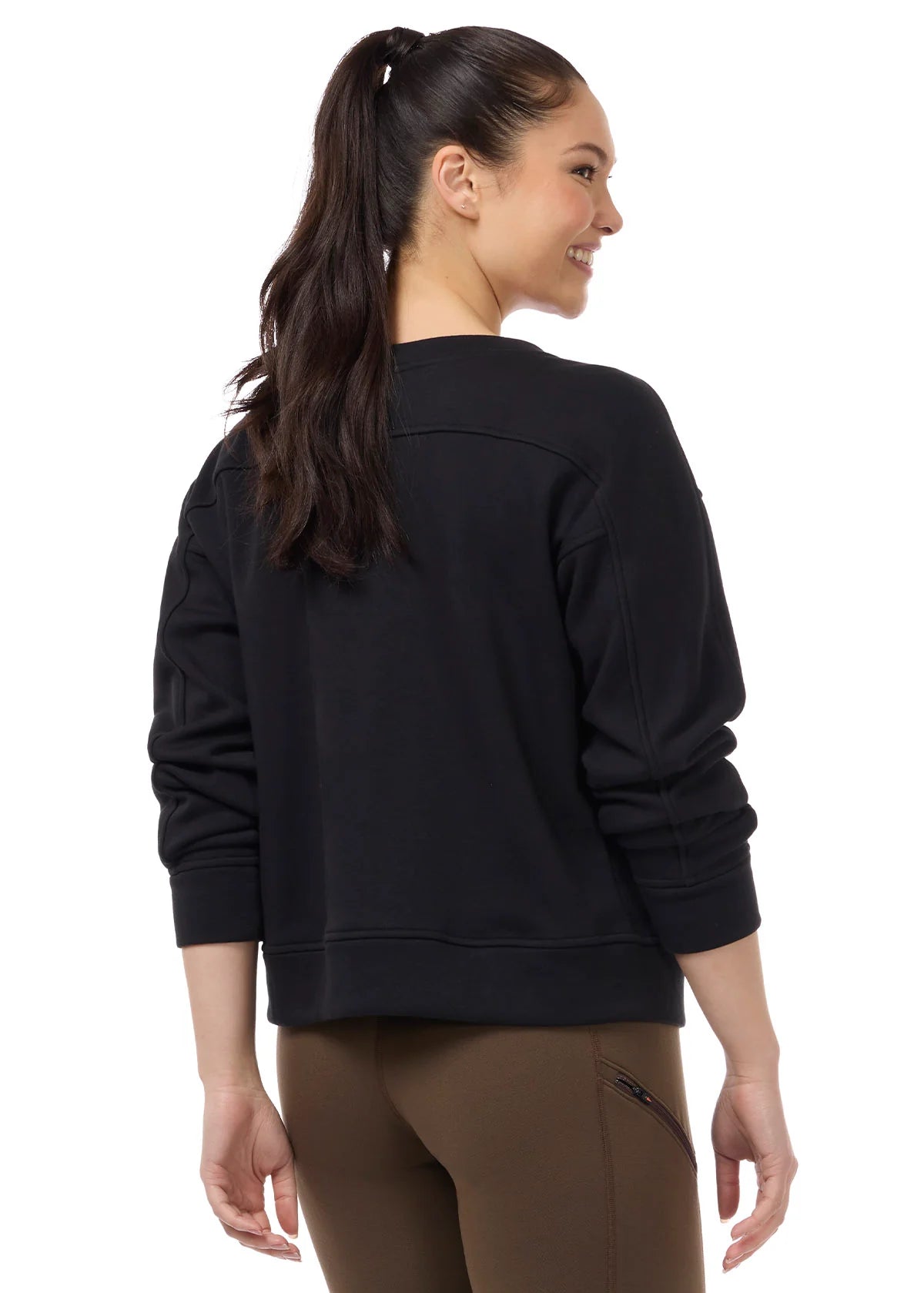 Back view of a female model wearing the Black Kerrits Cozy Crest Plush Fleece Sweatshirt on a plain background