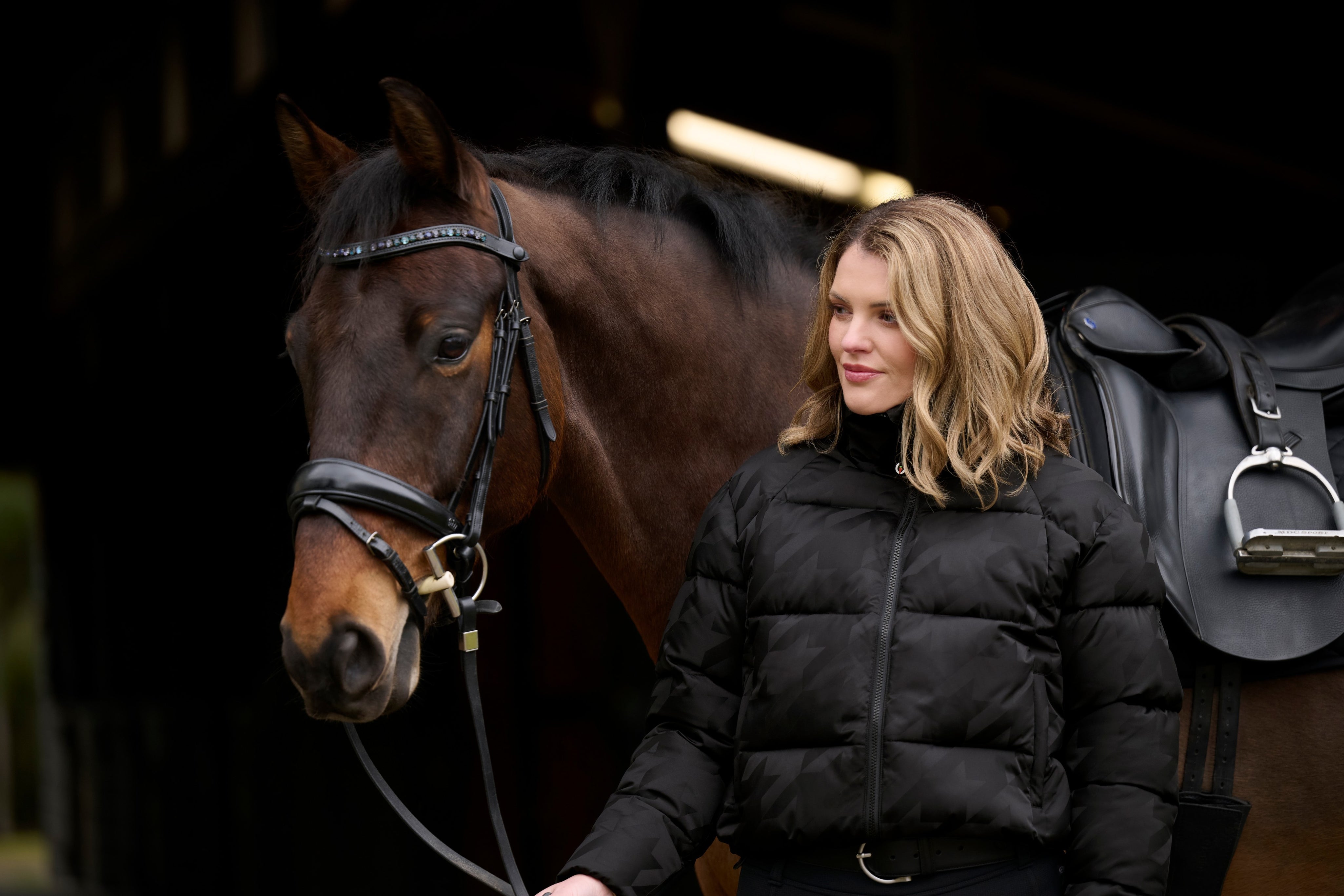 Front view of a model wearing Black Kerrits Skyline Houndstooth Puffer Jacket in front of a horse