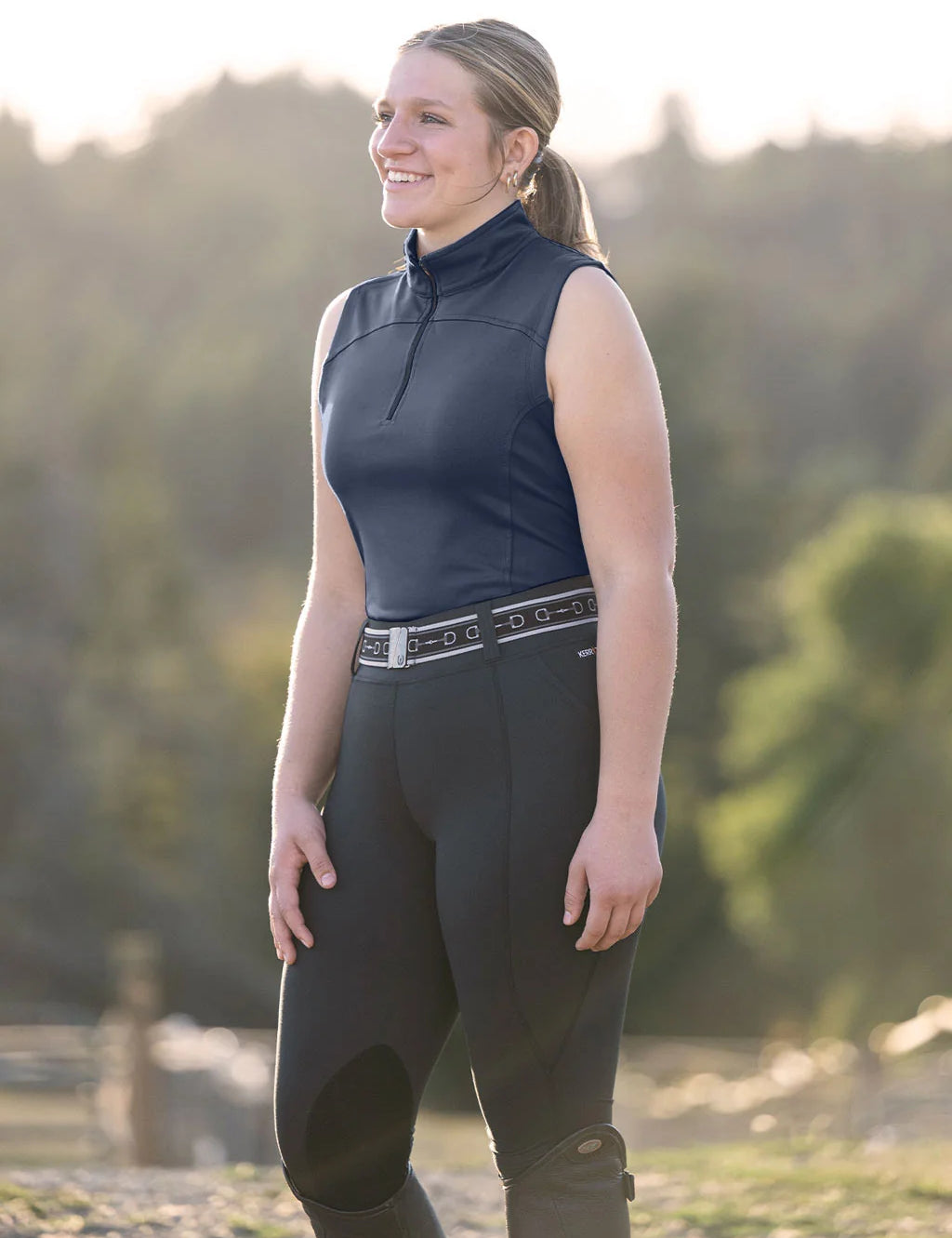 Angled front view of a model wearing the Neptune Kerrits Quarter Zip Performance Sleeveless Top while standing outside