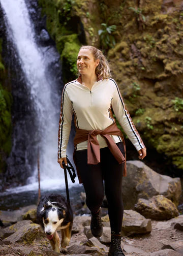 Woman walking outdoors wearing a light beige long sleeve riding shirt near a waterfall
