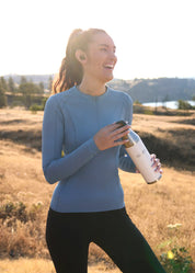 Woman wearing a blue long sleeve riding top holding a water bottle outdoors
