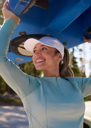 Front view of a female model wearing the light blue Kerrits Precision Long Sleeve Crew Neck Tech Top while holding a kayak above her head
