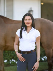 Front view of a female model wearing the white Criniere Margot Short Sleeve Show Shirt while standing in front of a bay horse