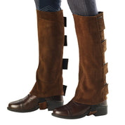 Side view of a model wearing the brown Ovation EZE Tab Suede Half Chaps over brown boots on a white background