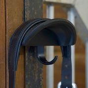 Close-up view of the black Correct Connect Magnetic Bridle Holder with Hook on a metal surface in a barn