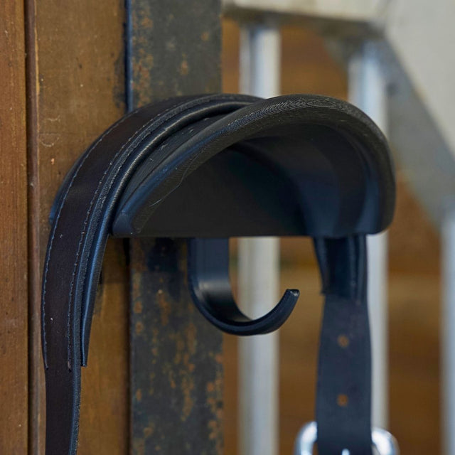 Close-up view of the black Correct Connect Magnetic Bridle Holder with Hook on a metal surface in a barn