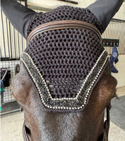 A horse standing in a barn wearing an ear bonnet with an AJ Equestrian Bonnet Bond Securing Strip seen through the crochet pattern