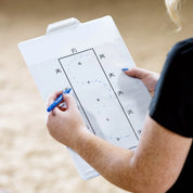 Over-the-shoulder view of a woman sketching a 3 loop serpentine with a blue marker on the Horze Learner Dressage Test Board