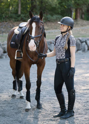 Full body front view of a female model wearing the black Kerrits Performance Knee Patch Pocket Tight while standing next to a horse