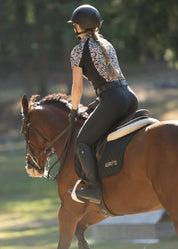Back view of a model wearing the black Kerrits Performance Knee Patch Pocket Tight while riding a bay horse