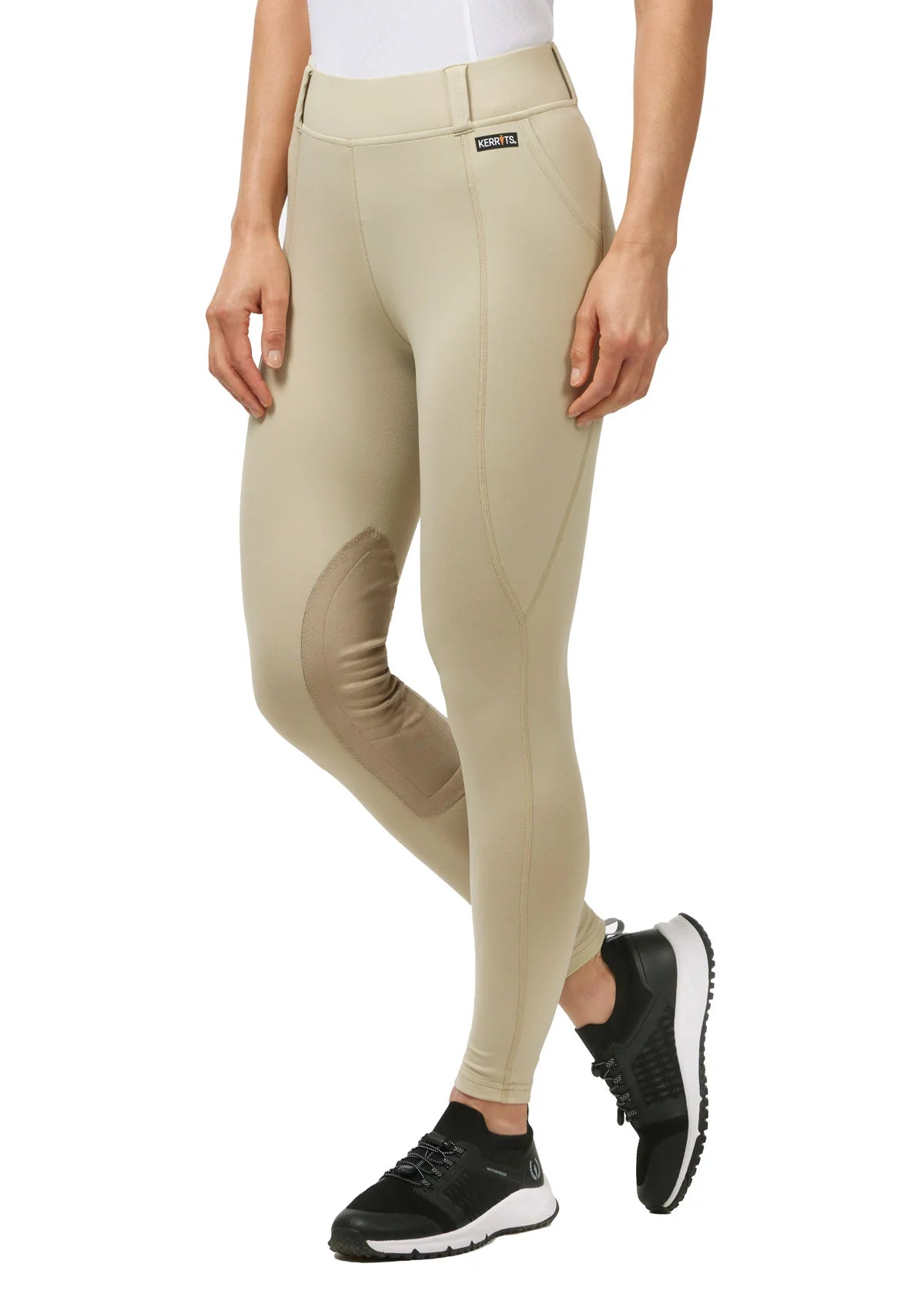 Angled front view of a model wearing the tan Kerrits Performance Knee Patch Pocket Tight on a white background
